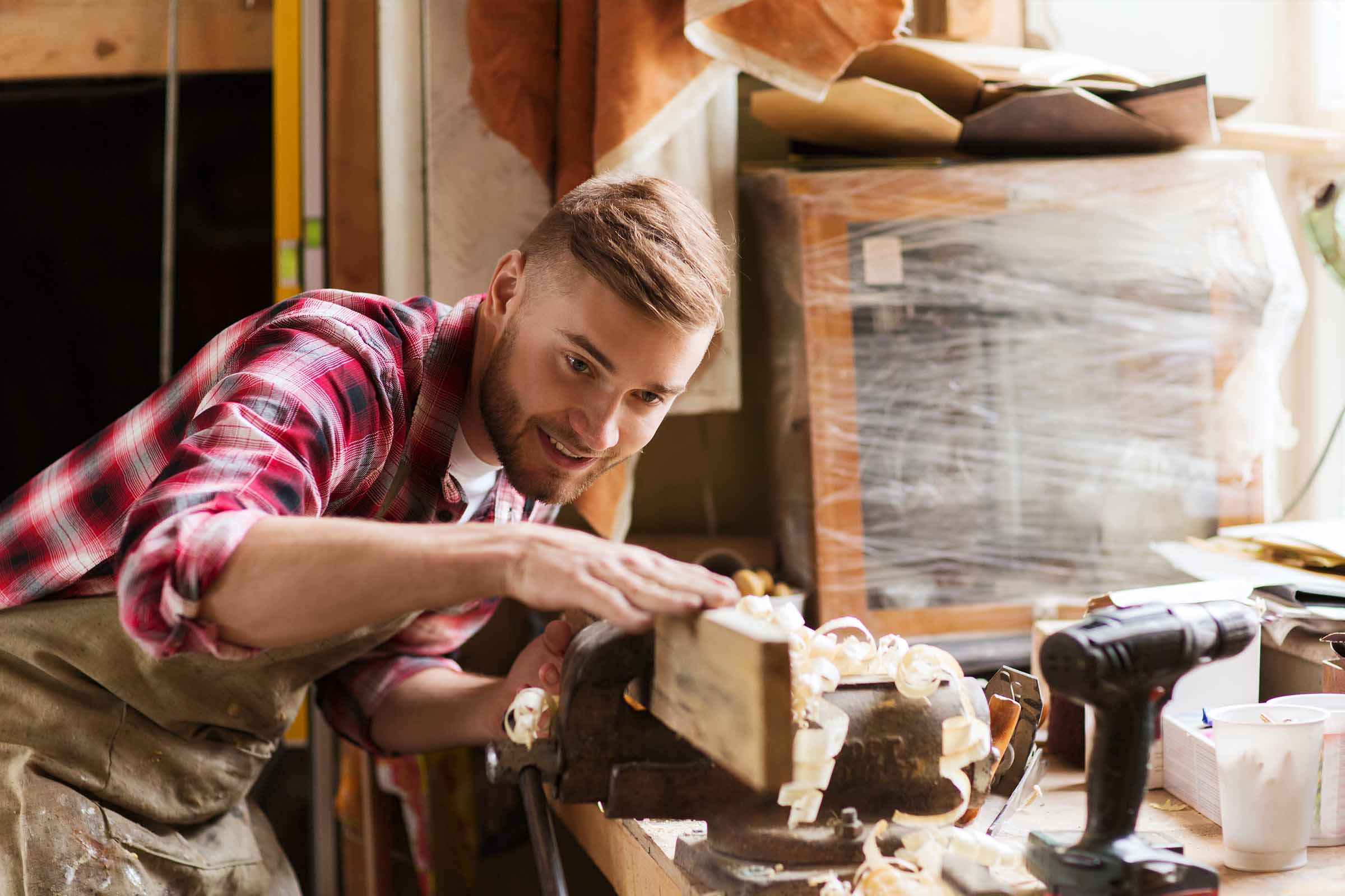 A man focused on crafting a wooden box in his workshop, surrounded by tools and wood materials